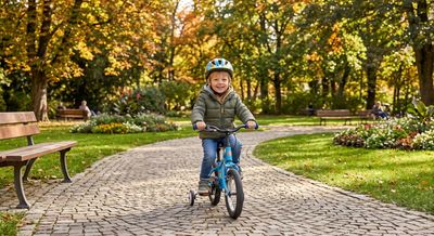 A young child riding a bike with training wheels along a park path in autumn